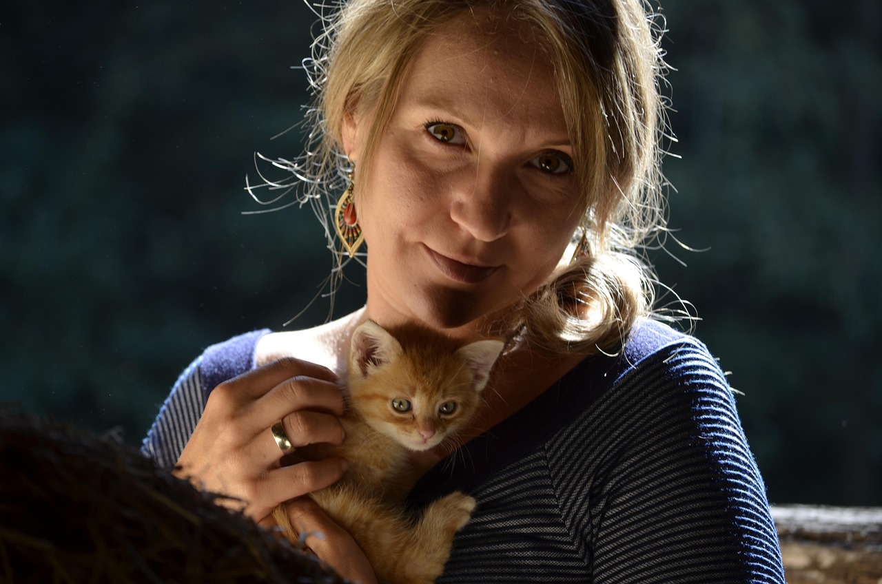 A woman sitting on the floor petting an orange kitten held against her shoulder