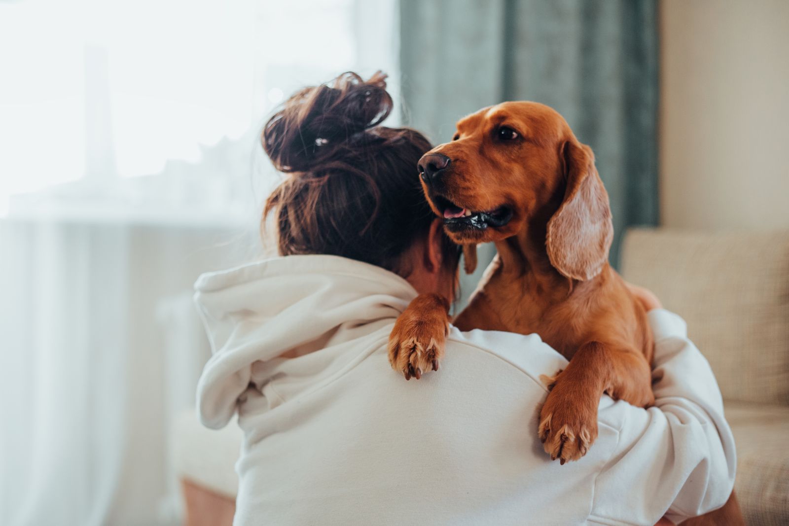 A woman in a white hoodie hugging a golden dog at home