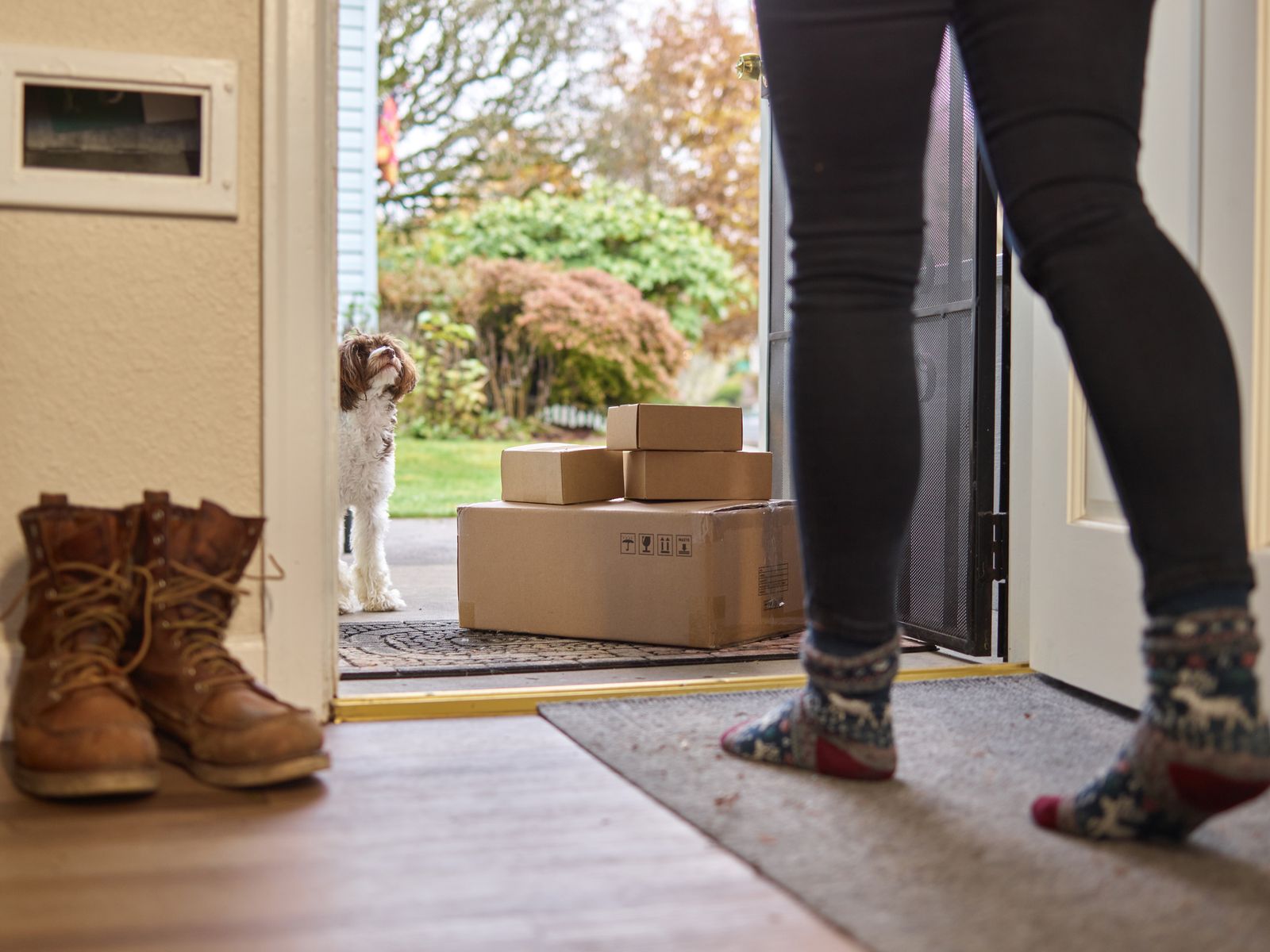 A dog peeking out of a doorway beside delivery packages on a doormat